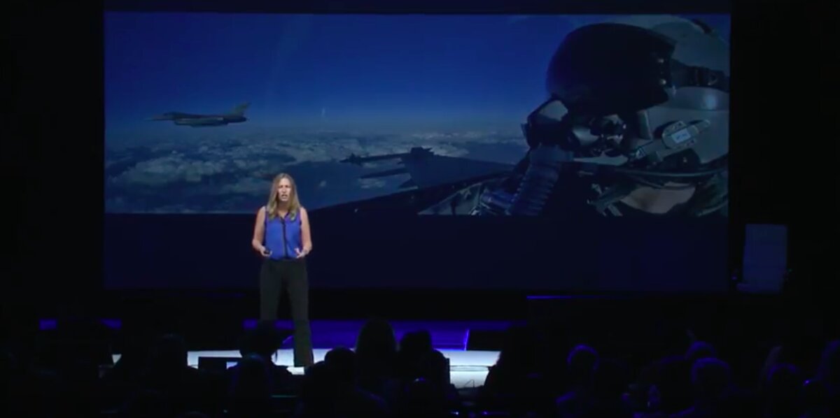 Ilana Golan telling her F-16 story on stage, with fighter jet cockpit footage on screen behind her